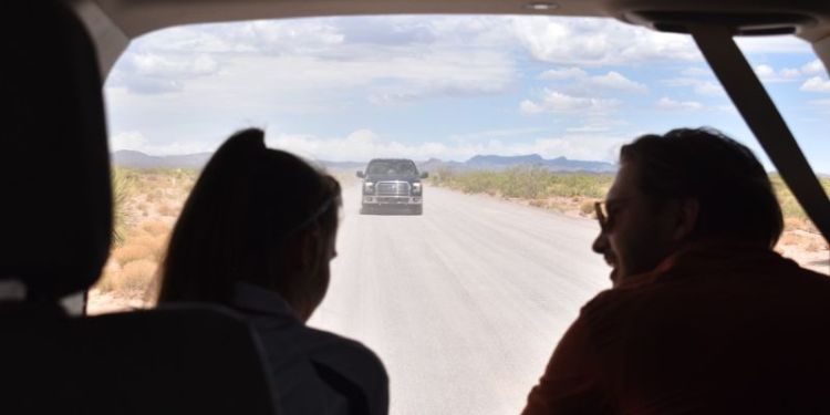 A photo of Freya Segar, left, and a fellow student, right, sat in a car. They are back lit and only their silhouettes can be seen. Behind them is the road and a car in the distance.