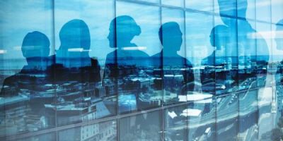 A photograph of a window showing the silhouettes of six people with a cityscape reflected in the glass.