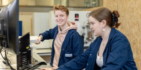 Two students wearing blue lab coats working on a Adibatic Compression work bench at the University of Leeds.