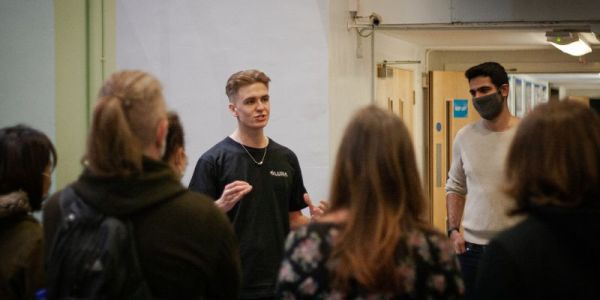 A photograph of Theo Youds giving a speech with 5 students stood around him.