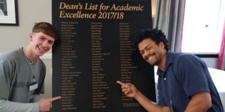 Benjamin Matheson and a fellow course mate stood next to the Dean's List board pointing to their names.