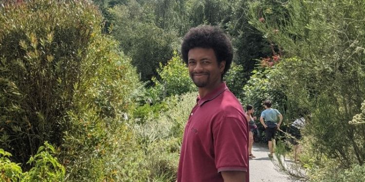 Benjamin Matheson stood looking at the camera surrounded by trees and bushes.