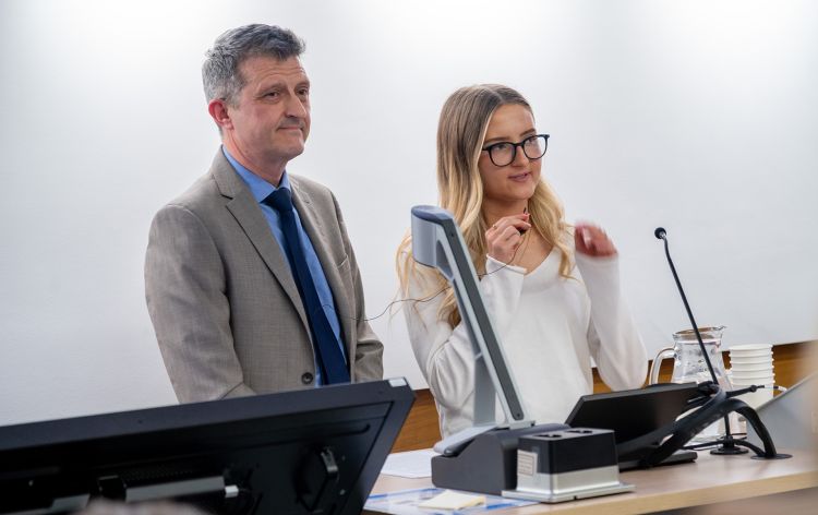 Mark McKelvie, Anne’s husband, and Rachel, her daughter, speaking to an unseen audience from behind a desk.