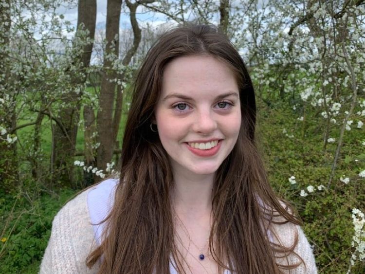 Female student smiling at the camera in front of a garden