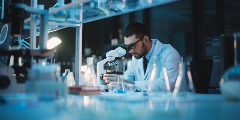 Scientist looking through a microscope in a dark laboratory